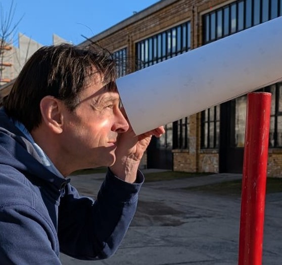 Person blickt in ein Sehrohr vor einem Industriegebäude